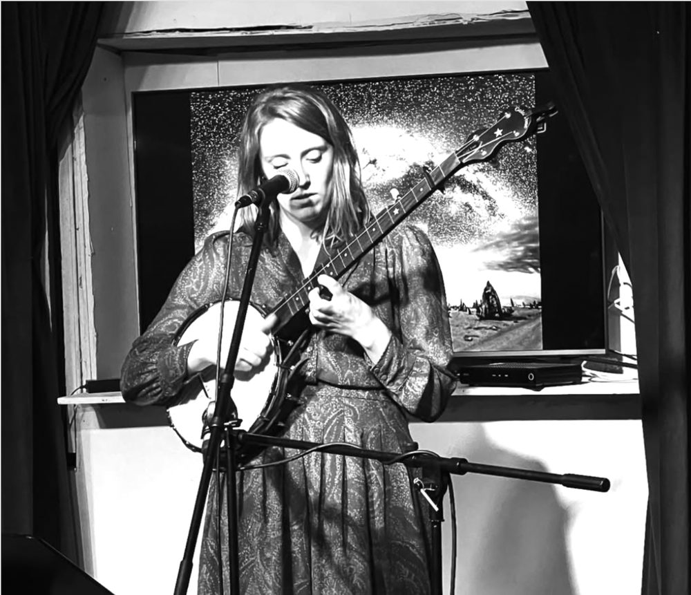 A banjo player singing on stage in black and white