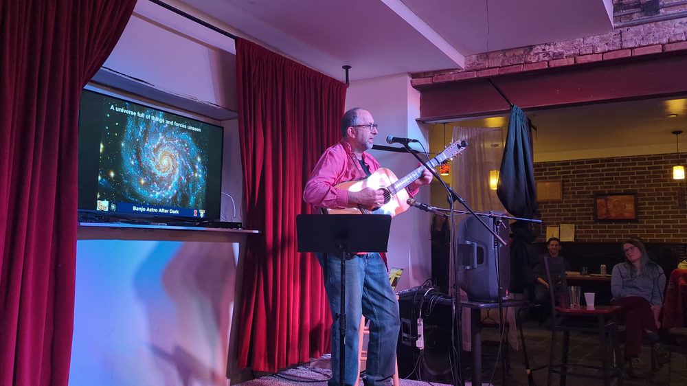 A guitarist singing in front of a spiral galaxy slide