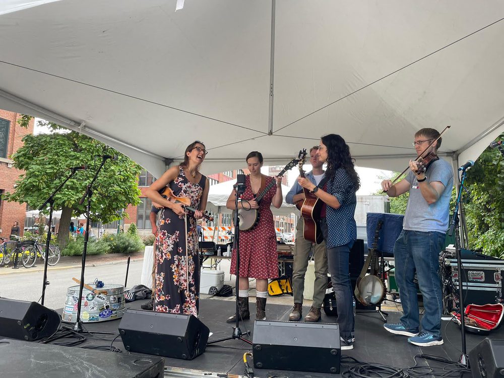 A folk band playing under a tent outdoors with Luke on fiddle