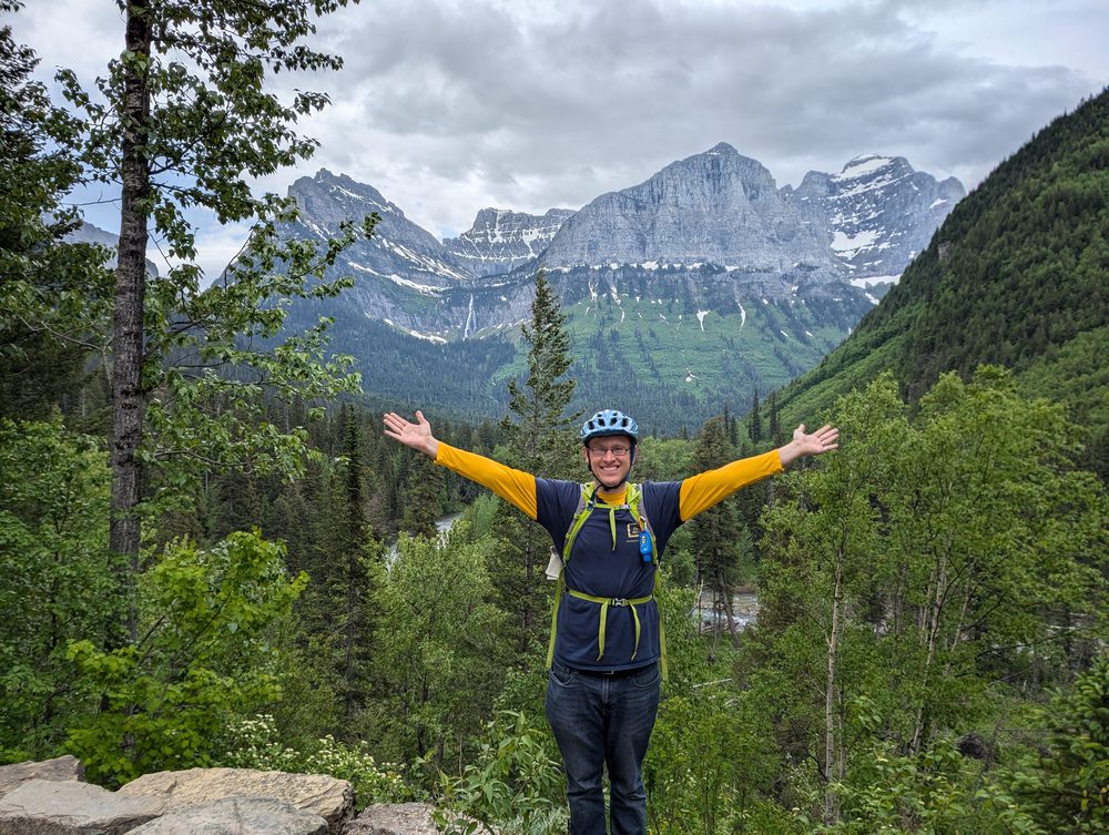 Luke with arms outstretched in front of snowy mountains
